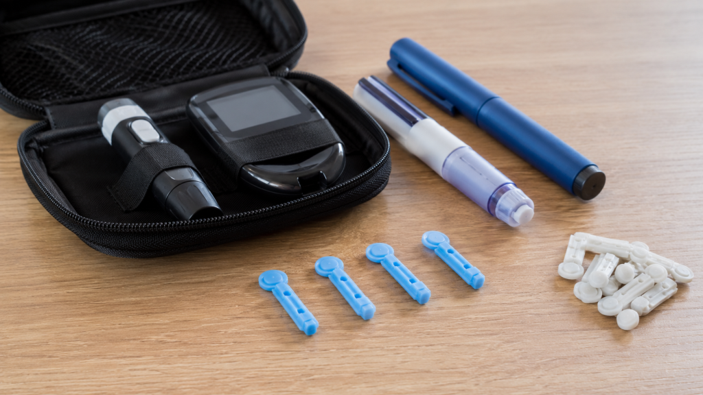 Na obrazie przedstawiono realistycznie zaaranżowany zestaw podstawowych akcesoriów diabetologicznych umieszczonych na jasnym drewnianym blacie